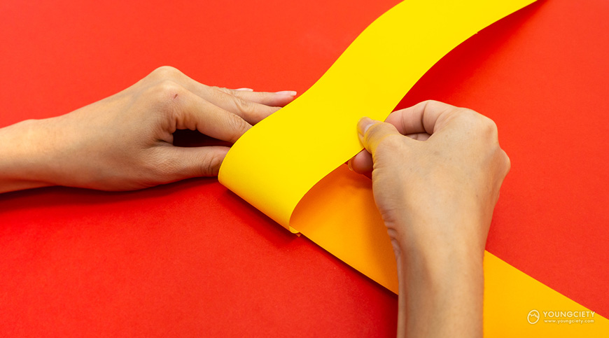  พับกระดาษสีเหลืองจากด้านล่างขึ้นไปทับกระดาษสีส้มด้านบน