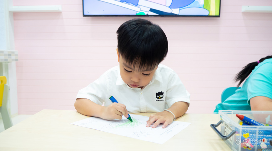 เด็กกำลังใช้สีเทียนสีเขียวระบายลงบนกระดาษ